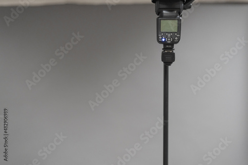 Camera flash light on the tripod on the gray background. © Natali