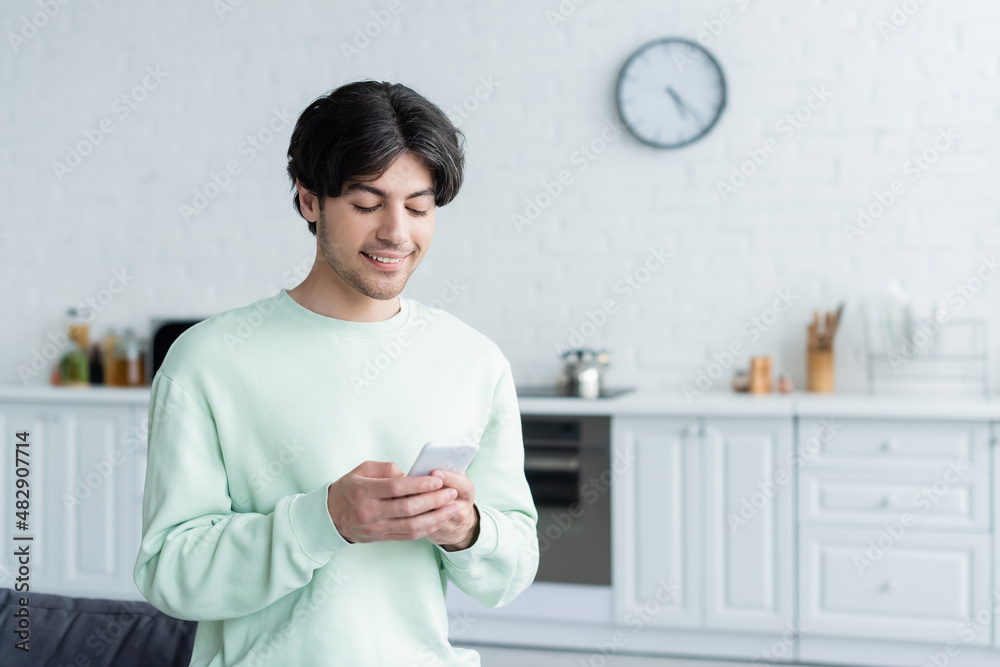 joyful man messaging on mobile phone in blurred kitchen. joyful man messaging on mobile phone in blurred kitchen.