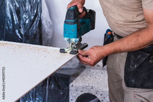 Carpenter cutting a wood board with an electric jigsaw. Home renovations.