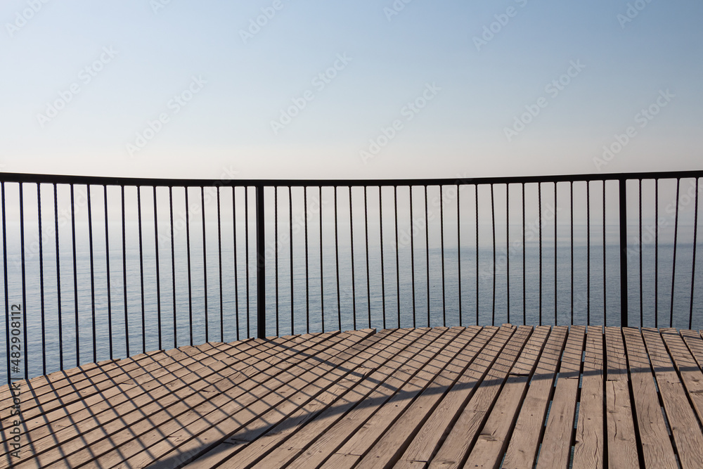 Beautiful wooden terrace with a metal fence is on the beach by the blue sea