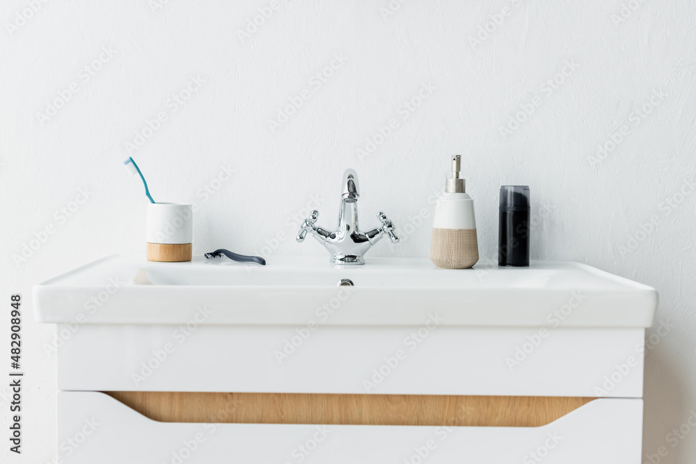 white sink with faucet, dispenser with liquid soap, shaving foam, safety razor and toothbrush. white sink with faucet, dispenser with liquid soap, shaving foam, safety razor and toothbrush.