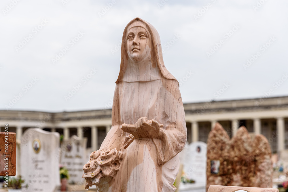 Marble sculpture of a caring virgin near graves in a Christian cemetery.