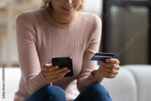 Close up female sit on sofa makes easy remote e-payment using smartphone and credit card. E-commerce client do shopping, buying goods and services on internet, easy money transfer, secure epay concept