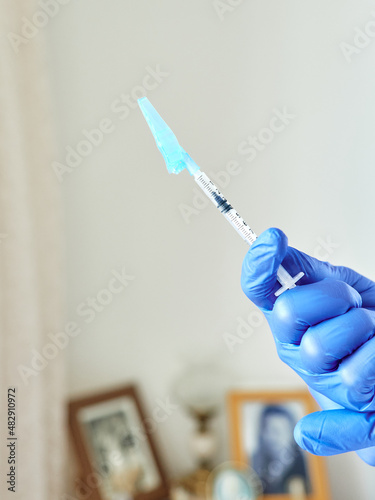 Doctor s hand holding an original syringe with blue adapter with covid-19 vaccine  inside a house