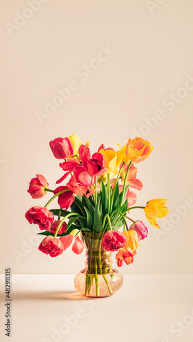 Big flowers bouquet of multicolored tulips in vintage glass vase on beige color background with copy space. Business card. Invitation postcard. Place for greeting text. International holiday. Banner.
