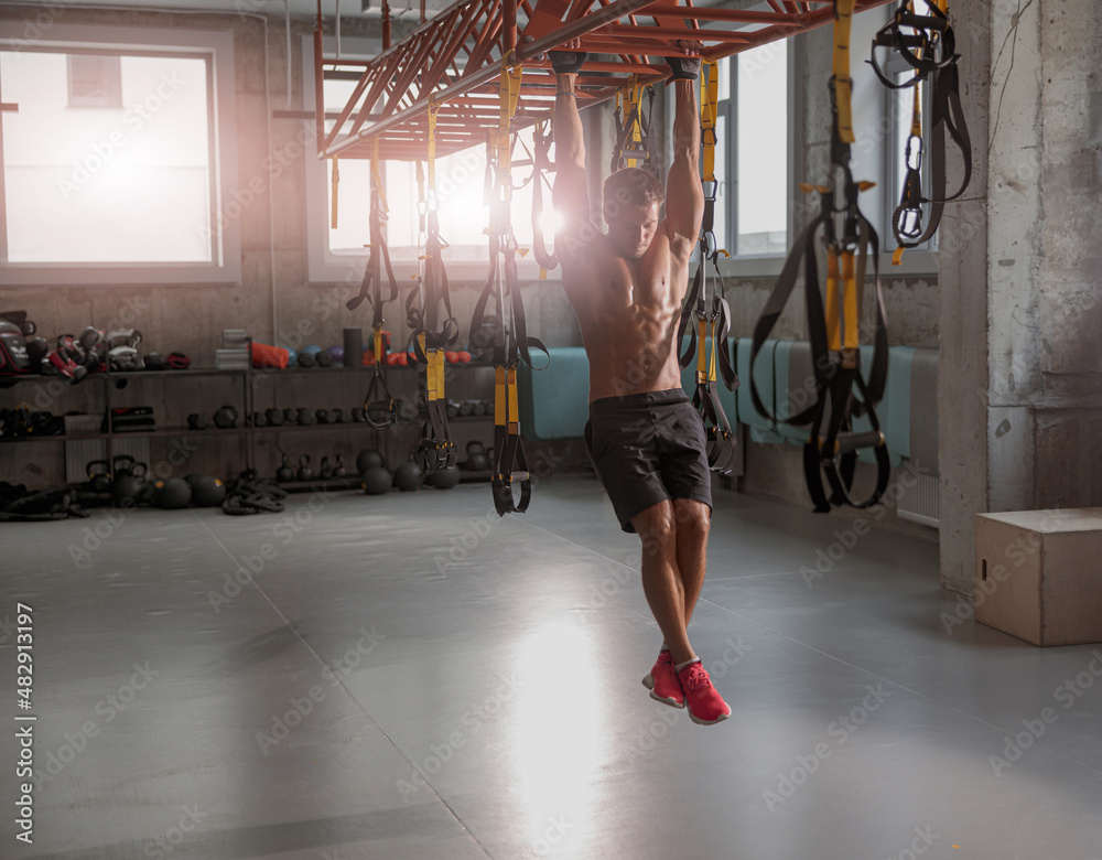 Obraz premium Young muscular man in gloves for training holding horizontal bar and performing exercise in the fitness club