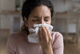 Unhealthy 30s Latina woman closed eyes blows runny nose in napkin, close up. Young allergic female suffers from seasonal allergy, catch a cold, influenza, health problems, chronic sinusitis concept