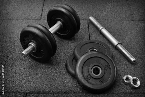 dumbbell and iron plates on the rubber floor in the gym. black and white photography. Bodybuilding equipment. Fitness or bodybuilding concept background.