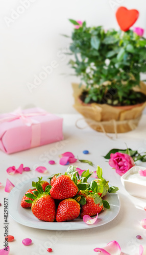 S.Valentine s Day concept. Strawberries on plate  wooden red heart  roses and its petals  gift