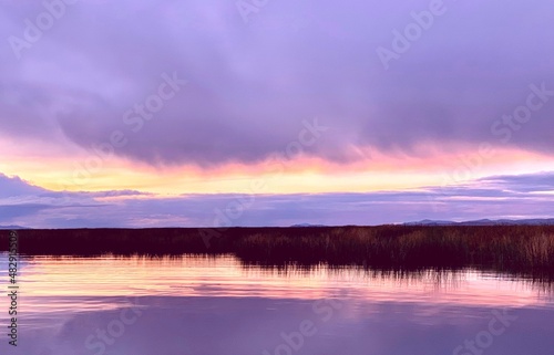 Violet sunrise over Titicaca lake at foggy morning. Beautiful clouds reflection in calm water. Idyllic scene. Tranquility. Zen. Harmony.