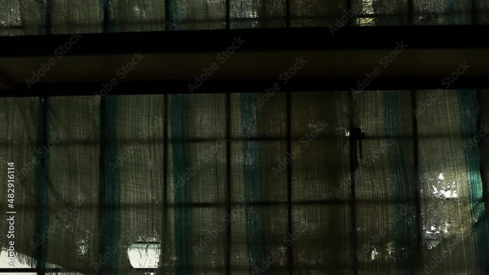 Metal bars on the window of an old industrial building. Dirty window of an abandoned building hung with torn cloth. Metal bars on the window of an old industrial building. Dirty window of an abandoned building hung with torn cloth.