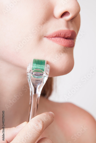 young redhead woman using a Clear and green derma roller for skin micro needle treatment photo