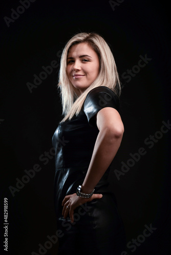 A beautiful blonde girl with long hair looks at the camera on a black background. Taken from the side