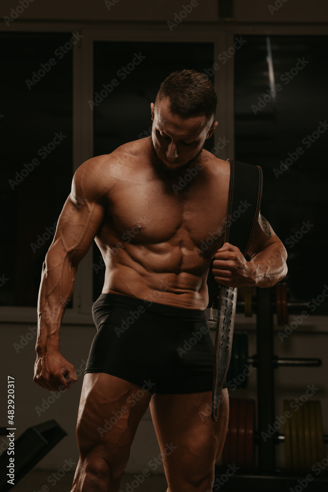 A shirtless bodybuilder with a beard is posing after a workout in a gym. A shirtless bodybuilder with a beard is posing after a workout in a gym.