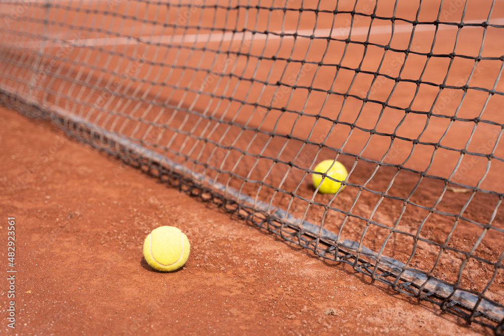 Two tennis balls separated by net on clay court. Sports tournament training concept
