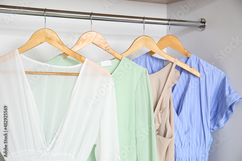 Stylish dresses hanging in wardrobe, closeup