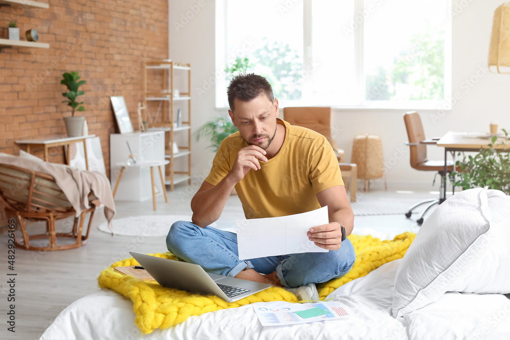 Thoughtful young man with document sitting on bed at home