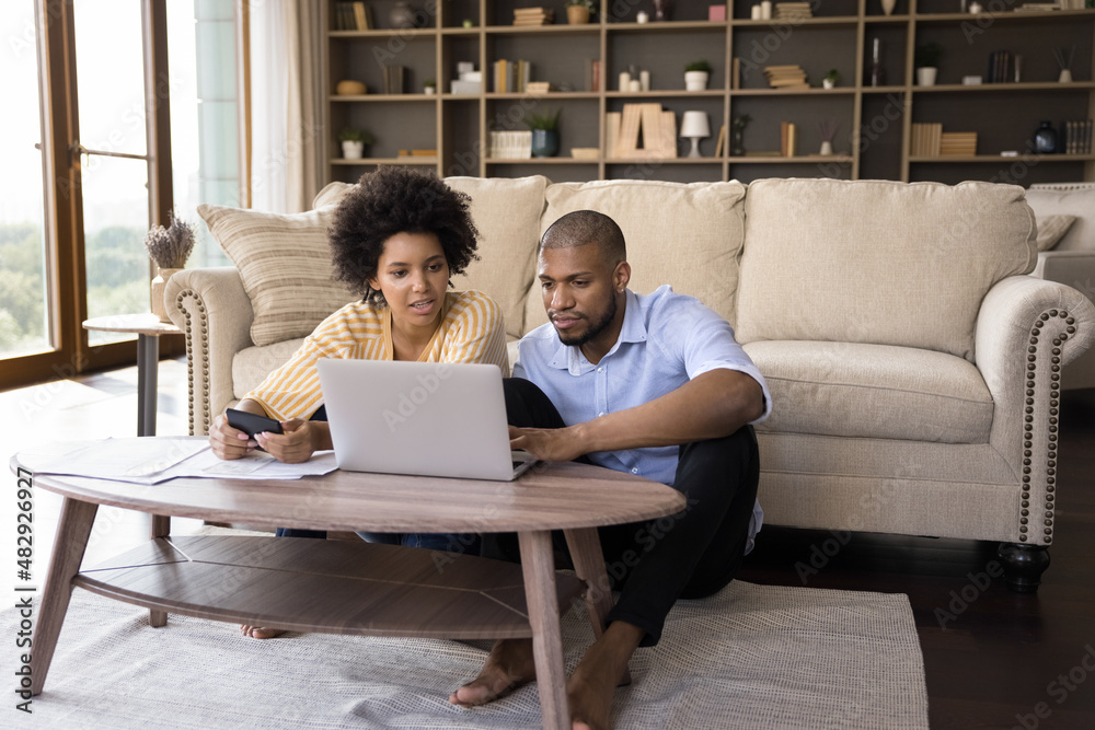 African couple sit in living room discuss receipts, control family budget, calculate household bills to pay, utility expenses, make payment via e-bank app on laptop, accounting, money control concept African couple sit in living room discuss receipts, control family budget, calculate household bills to pay, utility expenses, make payment via e-bank app on laptop, accounting, money control concept