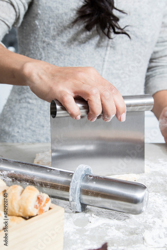 Woman uses a stainless steel French rolling pin and dough cutter to make baked pastries