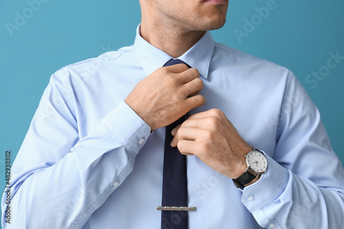 Young handsome man in formal clothes adjusting tie on color background, closeup photo