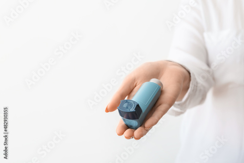 Woman holding asthma inhaler on light background