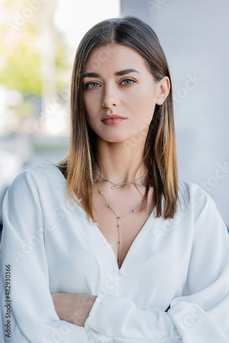 pretty young businesswoman with necklace standing with crossed arms in office.