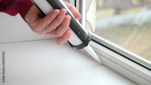 A man applies a sealant to the seam between the window and the sill from a tube of silicone sealant caulking with a gun. photo