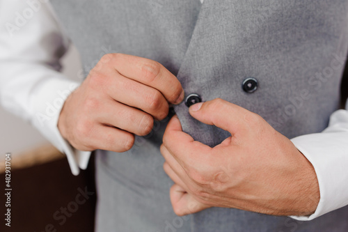 The man fasten a button on his jacket. The groom fasten a button on his jacket