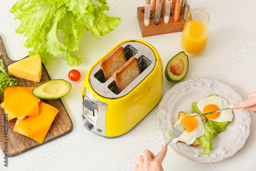 Woman having breakfast and yellow toaster with bread slices on white table