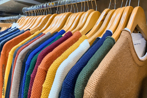 Sweaters of different colours on wooden hangers at clothing retail store or trift store. Clothing rental or donations, conscious and environmentally friendly consupmtion. Slow fashion concept photo