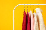 Clothes rack with knitted sweaters on color background