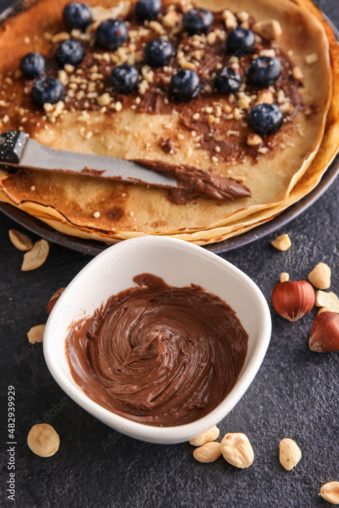 Bowl with tasty chocolate paste, nuts and crepes on black background Bowl with tasty chocolate paste, nuts and crepes on black background