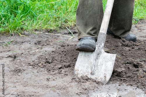 worker farmer man legs digging soil, ground with shovel in rubber boots in garden, close up