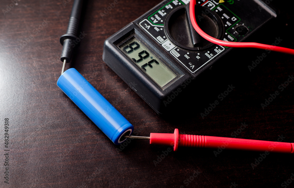 battery with volt calculator, voltmeter, red positive pole, black negative pole, on wood work table battery with volt calculator, voltmeter, red positive pole, black negative pole, on wood work table