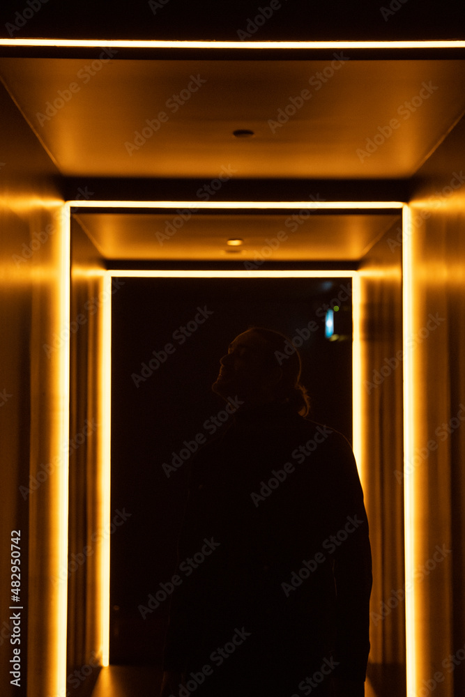 Personne debout dans la pénombre éclairée par des néons oranges. Homme qui observe l'architecture. Garçon dans l'ombre. 