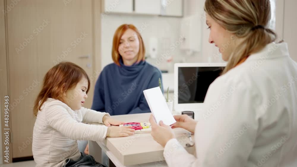 Pediatrician having session with female child in hospital office. Girl with mother visiting doctor. Medic is playing with young patient. Pediatrician having session with female child in hospital office. Girl with mother visiting doctor. Medic is playing with young patient.