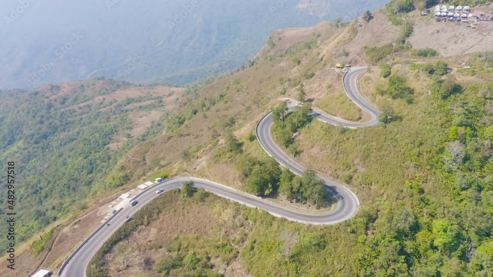 Aerial view of cars driving on curved, zigzag curve road or street on mountain hill with green natural forest trees in rural area of Nan, Thailand. Transportation. Aerial view of cars driving on curved, zigzag curve road or street on mountain hill with green natural forest trees in rural area of Nan, Thailand. Transportation.