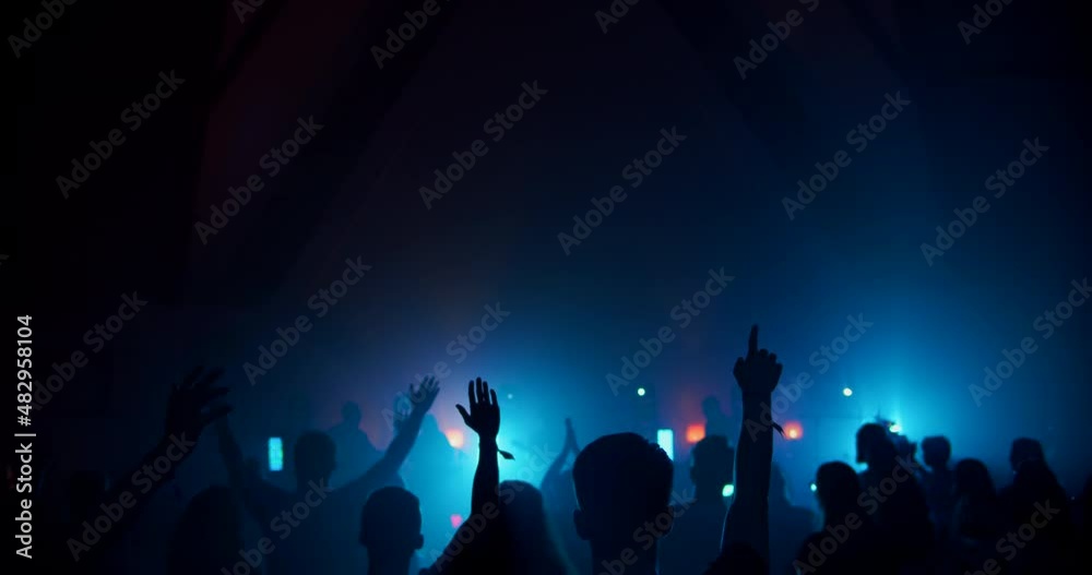 Rock or Pop Music Band on Illuminated Concert Stage with Crowds of Jumping and Applauding People. Festival Night Event Party with Light Show Performance. Background 4K handheld shot in slow motion Rock or Pop Music Band on Illuminated Concert Stage with Crowds of Jumping and Applauding People. Festival Night Event Party with Light Show Performance. Background 4K handheld shot in slow motion