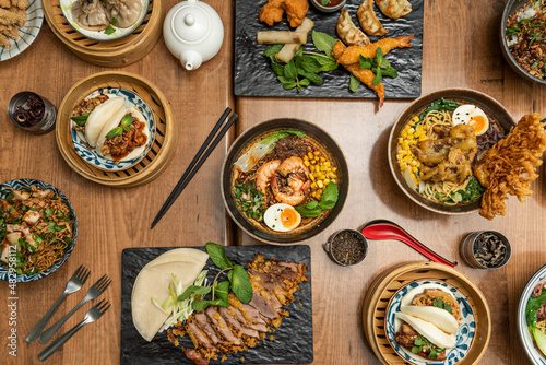 Set of asian food dishes with lots of ramen, bao bread, crispy duck, soy sauce, gyozas, spring and vietnamese rolls and boiled shrimp