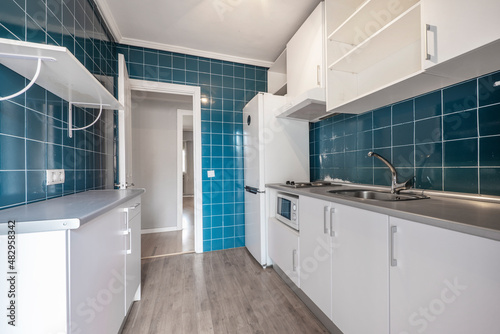 Conventional kitchen with white cabinets, gray countertop and small square blue tiles on the walls