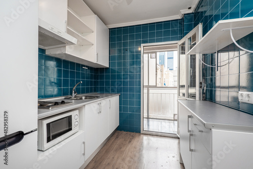 Kitchen With white furniture, gray worktop and small blue square tiles on the walls and exit to a glazed terrace