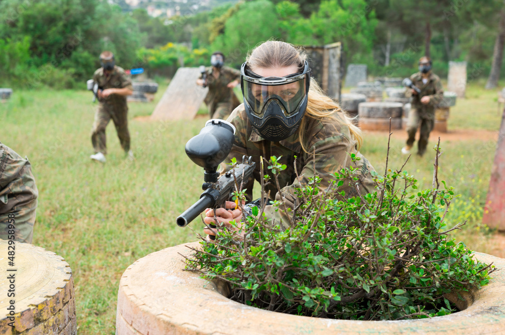 Fototapeta premium Female paintball player in protective mask with ammunition and gun on paintball field