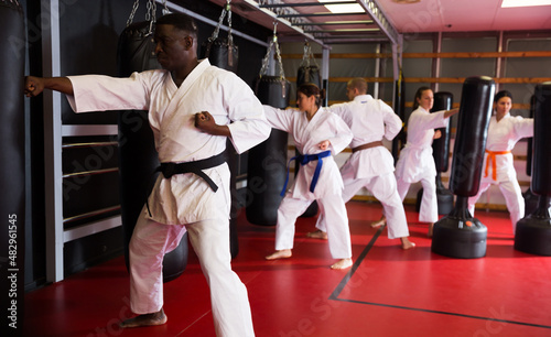 African-american man and group of people in kimono exercising with punching bags in gym during karate training.
