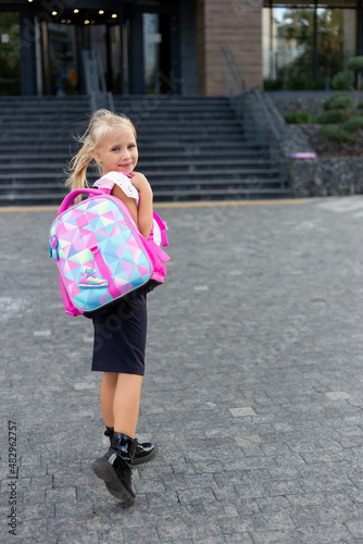 Back to school. Schoolgirl with backpack. Blonde girl goes to study. In uniform and with a school bag. Primary school, first grader, school student. © Alla