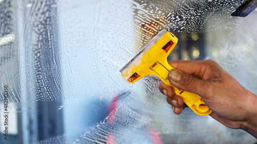 Razor handle to clean the windshield. Workers use a yellow scraper to scrape glue and dirt off the glass to clean before installing a new window film with a copy area. Selective focus