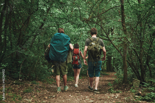 Three friends hiking down a trail through a forest, view from the back, using walking sticks, enjoying adventurous woods exploration © Teodor Lazarev