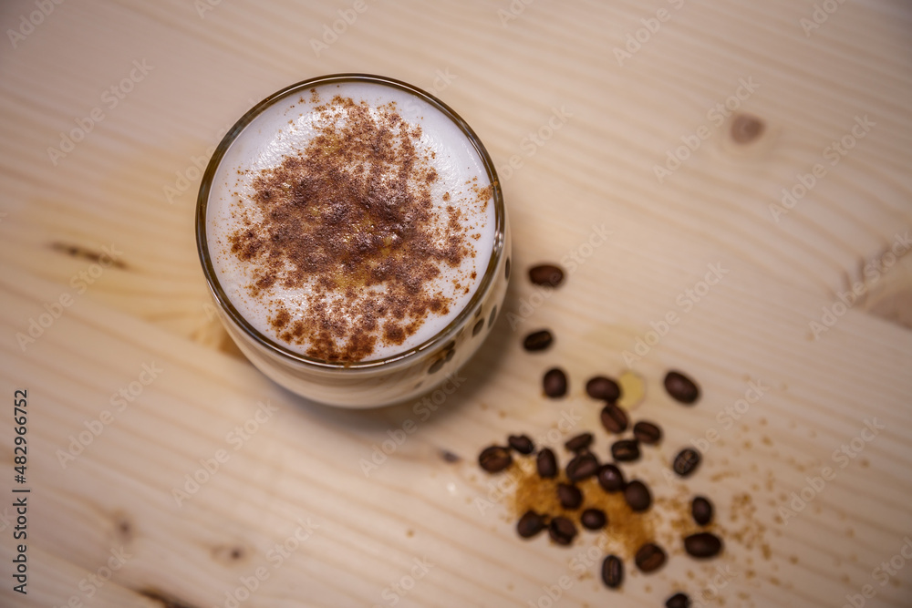 Layered coffee with cinamon in short glass from above on table with wood background and coffee beans Layered coffee with cinamon in short glass from above on table with wood background and coffee beans
