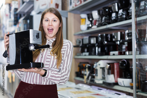 Positive female shop assistant showing coffee brewer in store of kitchen appliances