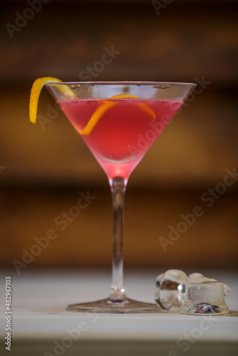 Fresh cosmopolitan martini in detail with lemon twist on table with wood background
