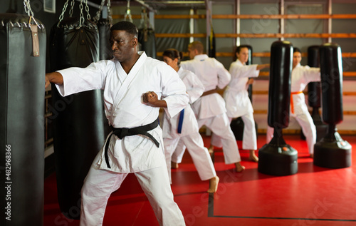 African american man in kimono practicing powerful body punches on heavy punchbag in gym